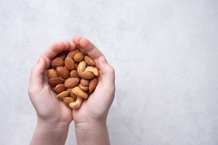 the child's hands hold a handful of nuts over a light gray background. Top view and copy spaceの写真素材