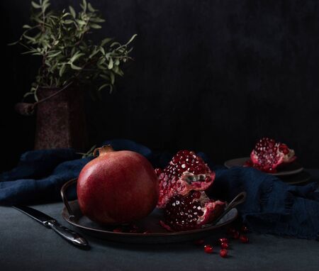a juicy  pomegranate lies on rustic  plate, vase and napkin  on a dark background. Dark and mood photoの写真素材