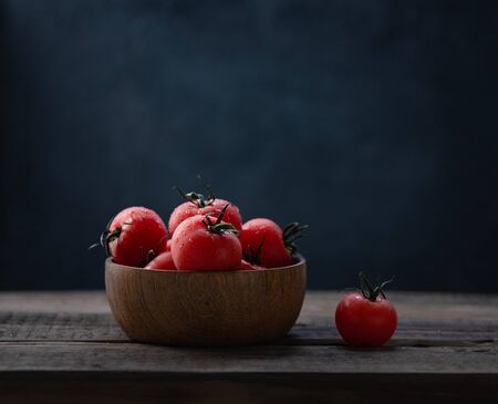 fresh sweet cherry red tomatoes in a wooden bowl on a wooden old table. Frontal and close-up view. Space for you textの写真素材