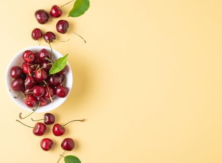 juicy cherries and leaves in white bowl on a yellow background. Top view and copy spaceの写真素材