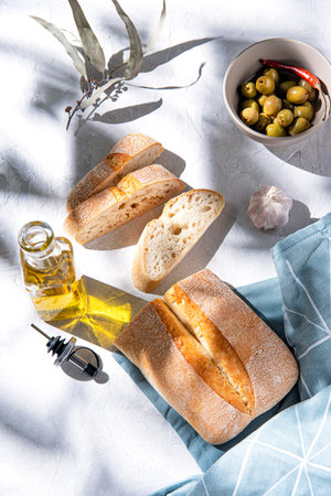 fresh baked bread lon the table with olives and oil in the morning sunlight. Top view