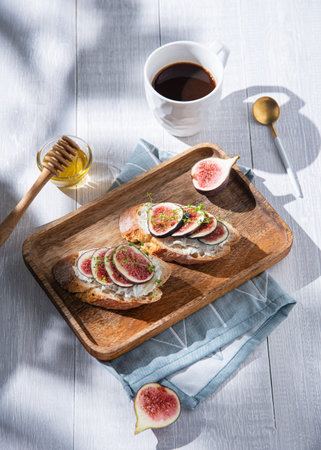 Breakfast with fig, cheese and honey sandwich on a wooden board and cup of coffee on white table, sunny morningの写真素材