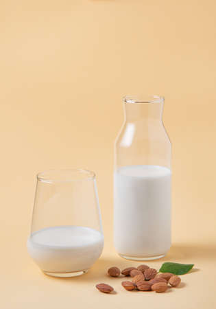 a glass and bottle of  vegan almond milk and a few scattered nuts on a yellow  background. Front view and copy spaceの写真素材
