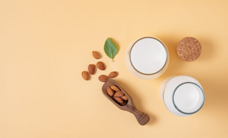 a glass and bottle of  vegan almond milk and a few scattered nuts on a yellow  background. Top view...