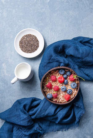 energy granola with raspberry,  blueberry and vegan milk into coconut bowl on blue background.  Top view and copy spaceの写真素材