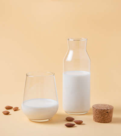 a glass and bottle of fresh vegan almond milk and a few scattered nuts on a yellow  background. Front view and copy spaceの写真素材
