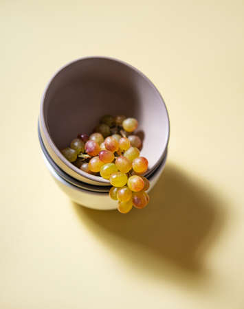 a cluster of juicy green pink grapes in a gray bowl  on a yellow background.  Top view and copy spaceの写真素材