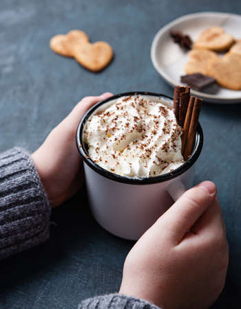a cup of hot chocolate with cream and cinnamon  in  woman hand on a dark  table with homemade cookies. Top view and close upの写真素材