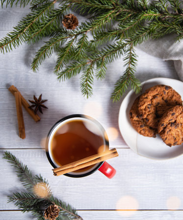 Flat lay christmas tea with cinnamon and spices in a red mug with homemade cookies on a wood background with a Christmas tree and a bokeh. Top viewの写真素材
