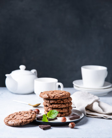 a  chocolate chip cookies with  nuts and mint with cup of tea and teapot  on a light table. Front view and copy spaceの写真素材