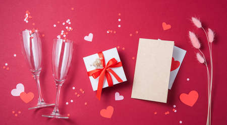 Flat lay of celebration. Two glasses, a gift box, a craft letter, flowers, papper hearts and confetti  on a red background. Concept of Valentine's Day, Mother's Day, wedding day. Top viewの写真素材