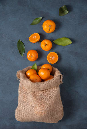 sweet tangerines with green leaves fall out of a crafting bag on a dark blue background. Dark photo. Top viewの写真素材