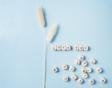 minimalistic flat lay with white dried flowers and scatter cubes with the word love you on blue...