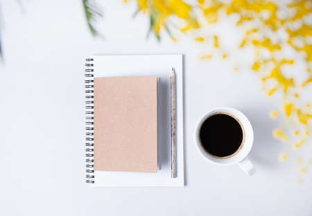 Flat lay with  yellow mimosa  flower, cup of coffee and craft notebook  on a marble table. Women's floral desktop. Spring morning concept. top view and copy spaceの写真素材