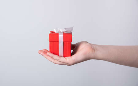 Women's hands hold a red holiday gift box with a white ribbon. Front viewの写真素材