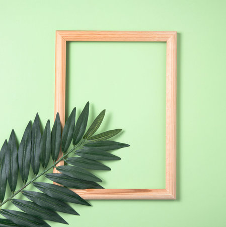 palm tree leaf and wooden frame on green background. Top view and space for text