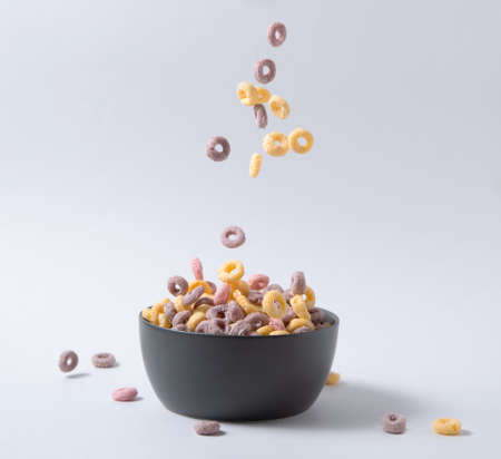 sweet colorful cornflakes rings fly in a black bowl on gray background. Front view and copy space imageの写真素材