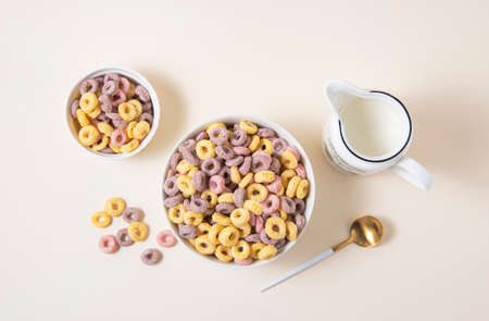 sweet colorful cornflakes rings in a white bowl with spoon and a jug of milk on a yellow background. Top view and copy space imageの写真素材