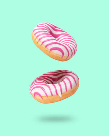 Two pink glazed  donut flying on neo mint background. Levitation concept food. Colorful imageの写真素材