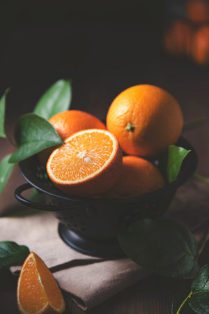 A few juicy oranges in a black bowl with green leaves on a dark wooden background. Dark, rustic and close up concept.の写真素材