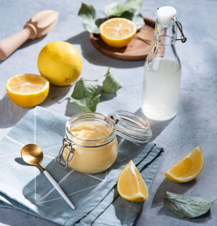 Delicious homemade lemon curd  in a glass jar with lemon slices and bottle juice  on a blue background. Concept breakfast with morning shadowsの写真素材