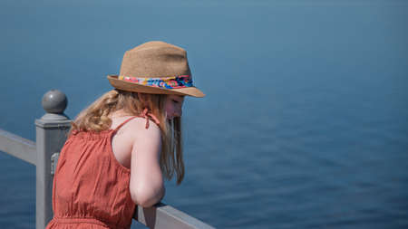 a girl stands on the seafront  and looks dreamily into the distance on a sunny summer day, without faceの写真素材