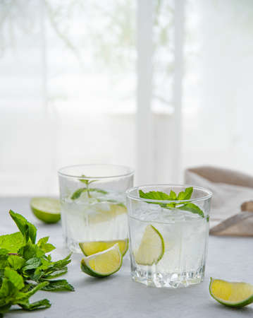 two glasses of lime lemonade mojito on the table with lime slices and mint in the morning light from the window. Front  view imageの写真素材