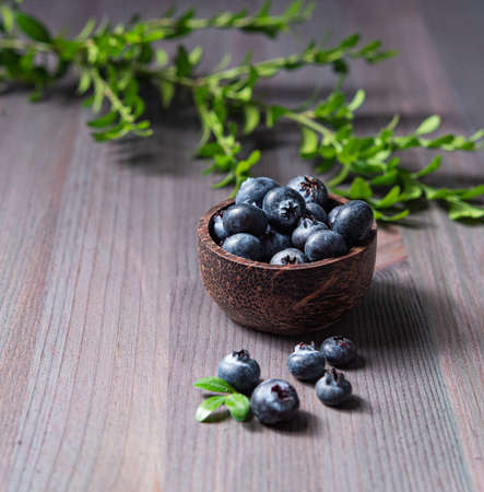 sweet fresh blueberries in a bowl  with green brunch on a wooden  background. Front  view and close up  imageの写真素材
