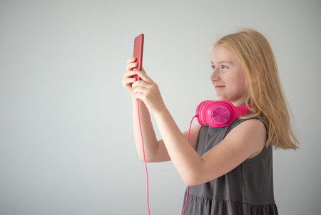 a girl in pink headphones and with a red phone on the gray background  takes photos