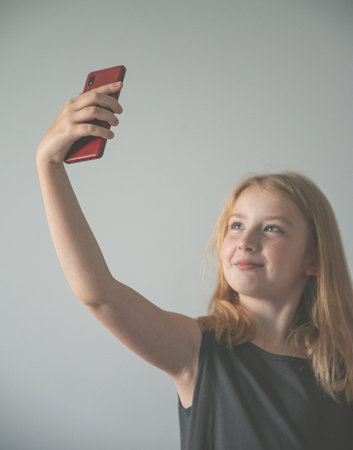a girl in gray dress  and with a  phone on the gray background  takes selfie. Tint image