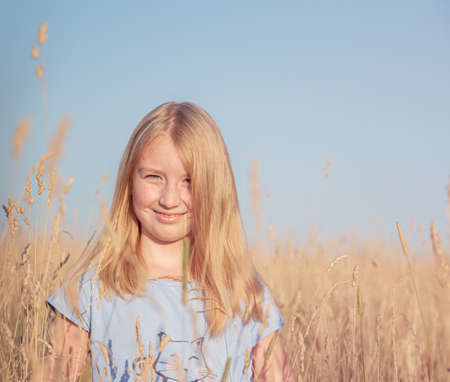 Portrait of a beautiful girl with golden hair in a blue T-shirt in a field with dry grass on  blue sky background. Copy space for text. Tint imageの写真素材