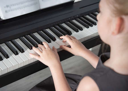 a girl in a gray dress plays an electronic piano  on a music book . Home Schooling Close up imageの写真素材