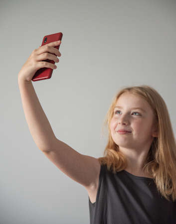 a girl in gray dress  and with a  phone on the gray background  takes selfieの写真素材