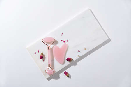 flat lay with pink gua sha for face massage and dry roses on white background with hard shadows. Top view and copy space imageの写真素材