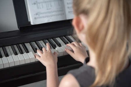 a girl in a gray dress plays an electronic piano based on a music book . Home schooling during the pandemic. Close up imageの写真素材