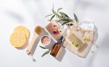 Zero waste concept beauty spa  with natural cosmetic products: soap, sponges, oil  and massage brushes, mineral salt on white  background with hard shadows and flowers.  Top view and copy space imageの写真素材