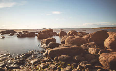 Beautiful sunrise on the shore of the Ladoga lake with stones and seaweed at sunny morning. Ladoga lake,  Karelia. Long exposure and tint imageの写真素材