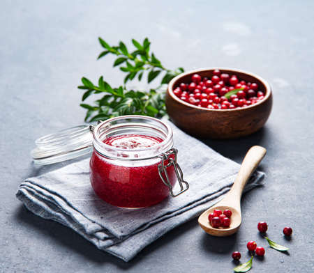 juicy forest lingonberry  in a wooden bowl and handmade jam in jar on gray background. Concept homemade healthy food. Close up imageの写真素材