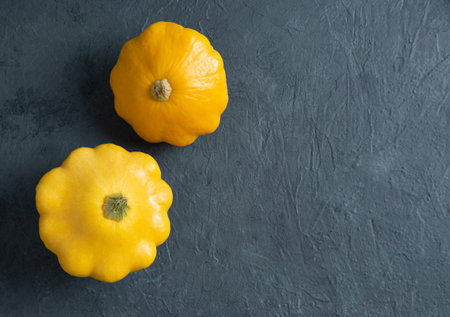 two yellow bush pumpkins on a dark textured background. Top view and copy space image