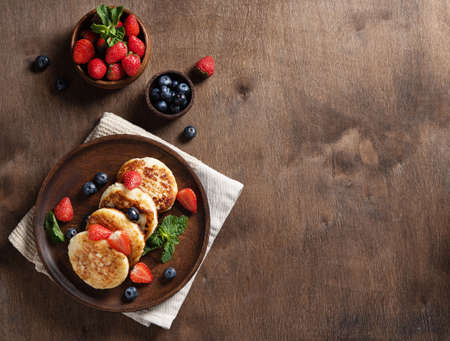 Cottage cheese pancakes or syrniki with blueberries, strawberries and fresh mint on a dark wooden background. The concept of a home-made healthy breakfast. Top view and copy space image.の写真素材