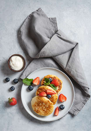 Traditional Russian dish for breakfast  syrniki. Cottage cheese pancakes with sour cream and fresh berries on a blue background with a napkin. Top view image. Vertical orientation.の写真素材