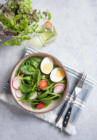Fresh salad of green spinach leaves, tomatoes, micro greens basil,boiled egg, red radish on light blue background. The concept of healthy, dietary and vegan food close up. Copy space  and top view.の写真素材