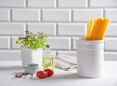 Raw spaghetti with tomatoes, basil, pepper and olive oil on a white brick background. Traditional ingredients for making Italian pasta. Front view.の写真素材