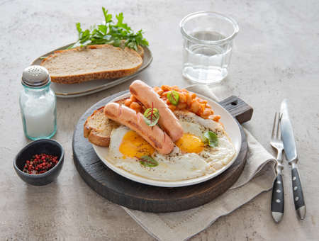 Traditional English breakfast with fried eggs, sausages, beans, fresh herb, red pepper and toast on a gray background. Concept morning food.の写真素材