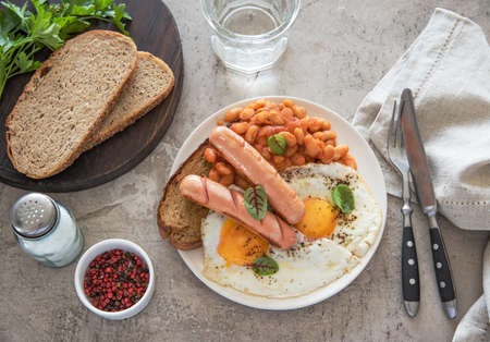 Traditional English breakfast with fried eggs, sausages, beans, fresh herb, red pepper and toast on a gray background. Concept morning and nutrition food. Top view.の写真素材