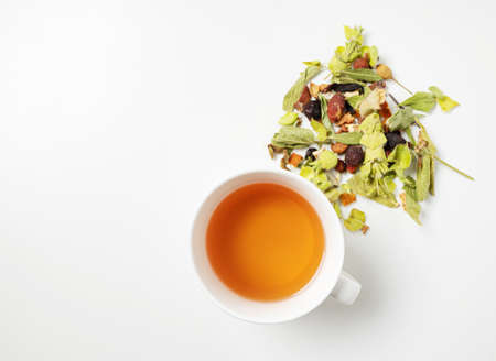 A cup of herbal tea with scattered dried herbs and pieces of fruit on a white background. Top view and copy space.の写真素材