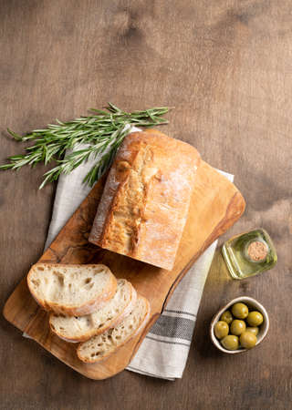 Fresh italian ciabatta bread cut  slices with rosemary and olive oil on wooden background. Top view  and copy space.の写真素材