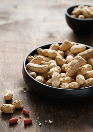 unpeeled peanuts in a black bowl on a dark wooden  background. Macro and close up image.