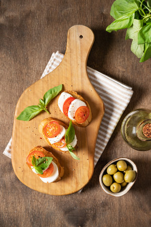 Caprese sandwiches with fresh tomatoes, mozzarella cheese and fresh basil and toast on a cutting board with spices and olive oil on a wooden  background. The concept of Italian food. Top view.の写真素材