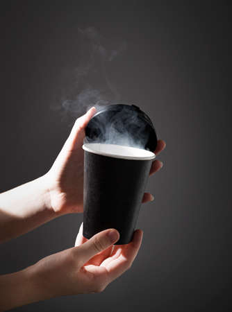 a black paper cup with aroma coffee or other drink in hands on a dark background with morning light. The concept of a cheerful morning.の写真素材